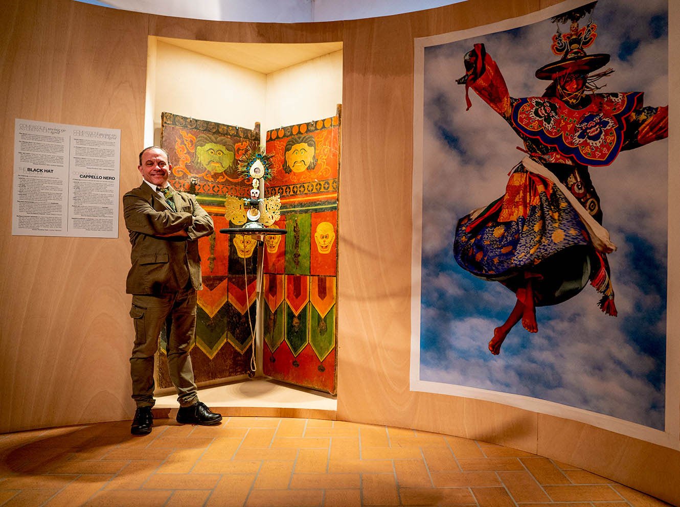 Core of Culture director Joseph Houseal stands in the galleries of Meditation in Motion, Footsteps to the Sublime, next to a goenkhang door from the altar room of the most ferocious protective deities, and a Black Hat sorcerer's hat. A large photo image by Herbert Migdoll of a dancing monk wearing a Black Hat hangs next to the installation.